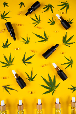 Cannabis leaves and CBD oil in small bottles on yellow background.の写真素材