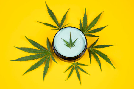 Cannabis cream with marijuana leaf on yellow background, top viewの写真素材