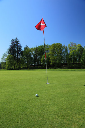 golf ball next to a flag on a green of a beautiful golf course with dramatic summer skyの写真素材