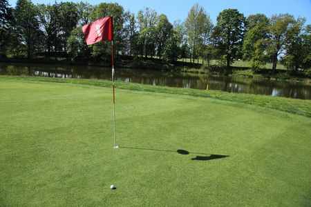 golf ball next a flag on a green of a beautiful golf course の写真素材