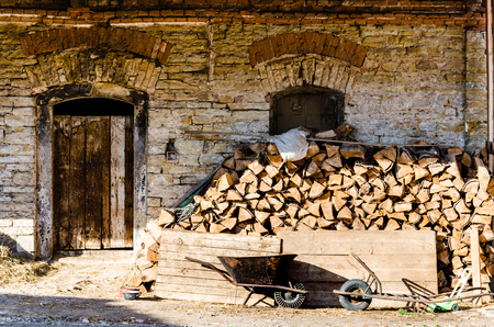 Very old brick wall with wooden door on very old farm. Stack of logs behind the wall.の写真素材