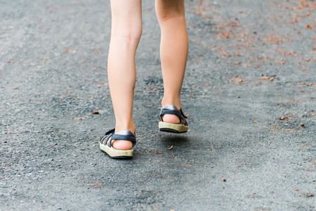 Step of young girl. Legs in sandals, step on the asphalt road. Autumn leaves on background.の写真素材