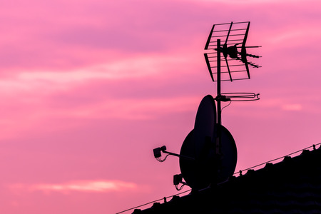 Silhouette of roof with satellite and antenna on nice vibrant violet and pink sky. Beautiful colored sunset.の写真素材