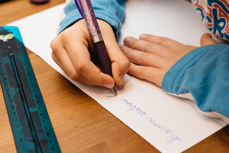 Child doing homework. A young girl writes on paper and uses a pen.の写真素材