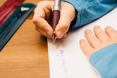 Child doing homework. A young girl writes on paper and uses a pen.の写真素材