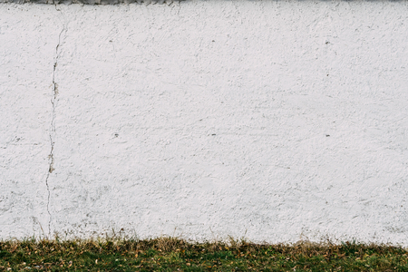 Pure white wall with texture. Blue sky with clouds at the top part, green grass at the bottom part.の写真素材