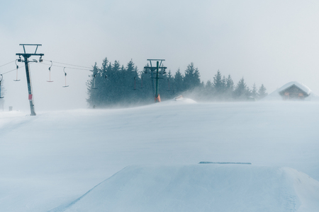 Strong wind on the top of ski slope in winter.  A lot of snow. Surface lift T-bar, mountain cottage on horizon.の写真素材