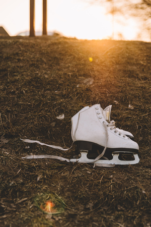 White lady's ice skates lying on the ground. Beautiful sunset on the background. Beautiful yellow soft light.の写真素材