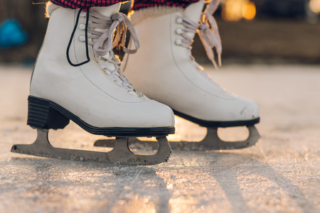 Close-up of woman skating on ice. Close-up of skates and ice. Side view. Beautiful winter sunset on background. Golden light.の写真素材