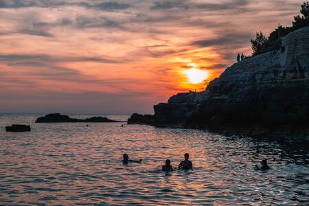 Silhouettes of unrecognizable people in the water and on the rocks by the sea.の写真素材
