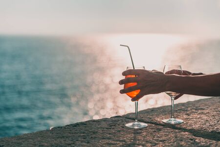 Hands holding two glasses with alcohol. In the background you can see the open sea and the horizon.の写真素材