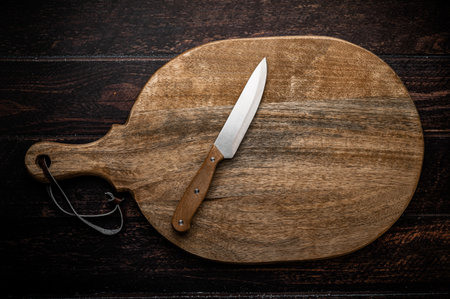 A large wooden cutting board with a knife on a dark wooden table.の写真素材