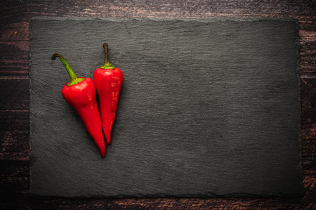 Three hot chili peppers on a slate board on a dark wooden table.の写真素材