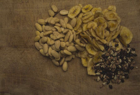 The mix of dried banana slices, chocolate beans and almonds on the wooden dick from a top side of view.の写真素材