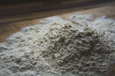 The small hill made of flour on the old wooden plate in the kitchen prepared for baking a bread.の写真素材