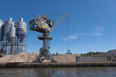 Bulk-handling crane unloading sand, road metal and gravel from cargo vessel ship, heavy vehicle and...