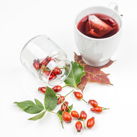 Bunch of rose hips spreaded on white background with rose hip tea and autumn leavesの写真素材