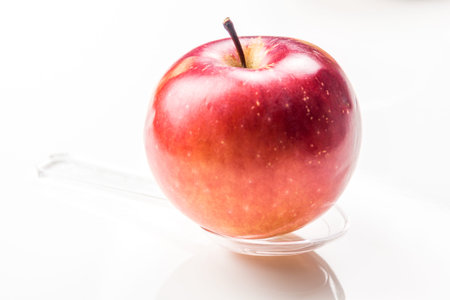 red apple on translucent medicine spoon on the table symbolizing that drinking and eating of apple products prevents diseases and is full of vitaminsの写真素材