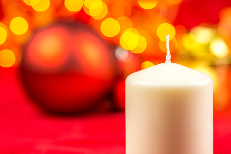 White christmas wax candle and balls on red background with bright yellow lightsの写真素材