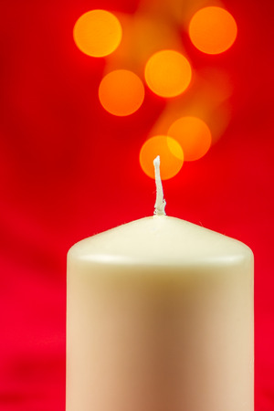White christmas wax candle on red background with bright yellow lightsの写真素材