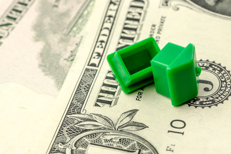 two little green houses made of plastic are laying on their roofs on dollar banknotes, business conceptの写真素材