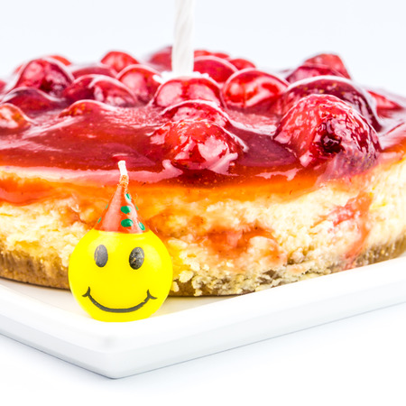 cheese cake with strawberry and funny laughing candles on white backgroundの写真素材