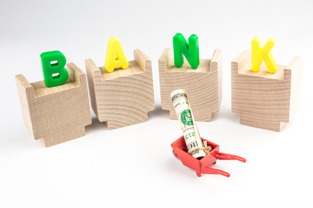 bank concept, miniature of wheelbarrow with dollar banknote standing in front of bank buildingの写真素材