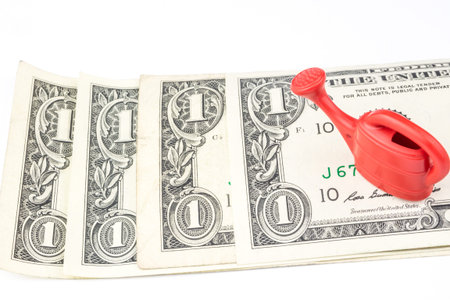 one red watering can laying on four one dollar banknotes on white backgroundの写真素材