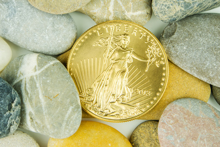 golden ounce of american eagle coin hidden under pebble stonesの写真素材