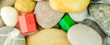 two red and green miniatures of plastic houses laying under differrent pebble stonesの写真素材