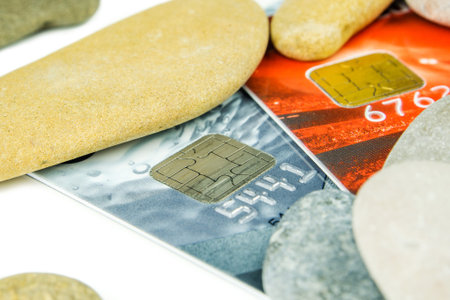 grey and red debit cards are laying under various pebble stonesの写真素材