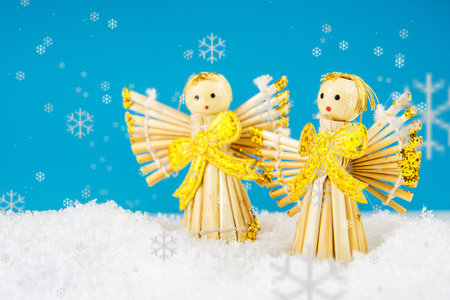 two straw angels laying on snow with turquoise background
