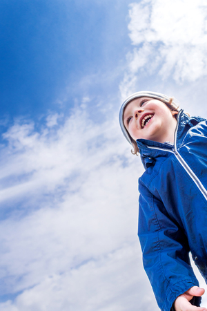 young handsome boy laughing and enjoying his stay on fresh air with blue cloudy sky in the backgroundの写真素材