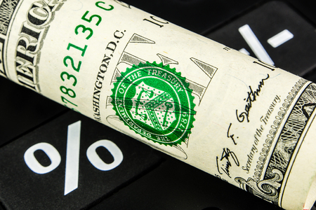 one american dollar banknote rolled is laying on white percentage button of black calculatorの写真素材