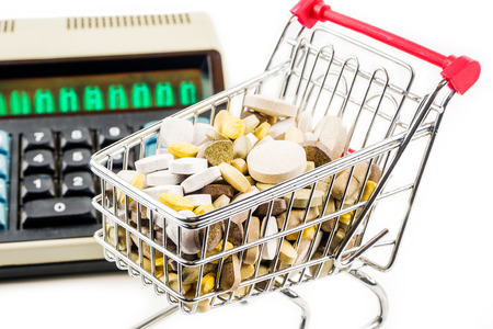 shopping cart full of vitamin supplements on white background with retro calculator in the backの写真素材