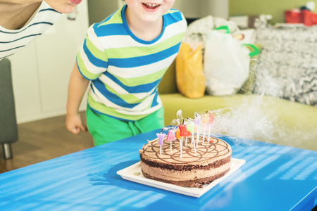 birthday party with chocolate cake with candles in form of letters with young boy moving around blue wooden table, happy birthday theme, young boy trying to blow  candlesの写真素材