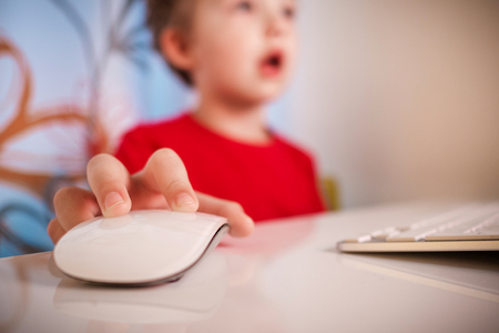 closeup view of young boy playing with computer at night lit by the light form the screen with blurred face and focus on computer mouseの写真素材
