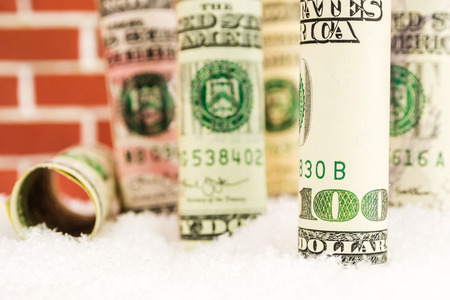 american dollar banknote rolls in all denominations covered with snow on red brick wall backgroundの写真素材