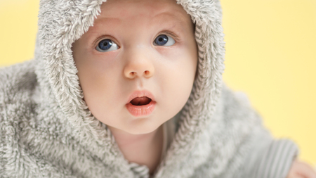 closeup of beautiful happy baby with blue eyes in grey bear like clothing on yellow backgroundの写真素材