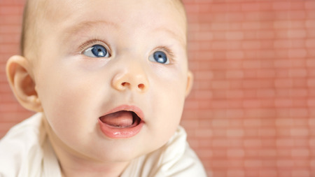 closeup of beautiful happy baby with blue eyes on red brick backgroundの写真素材