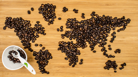 map of the world made of roasted arabica coffee beans laying on bamboo wooden textured backgound with white ceramic cup full of roasted coffee beansの写真素材