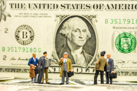 business concept, closeup of miniature figurine of businessmen discussing on us dollar banknotes...