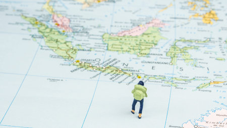 closeup of miniature figurine of young traveler standing on big map next to Indonesia, Bali island