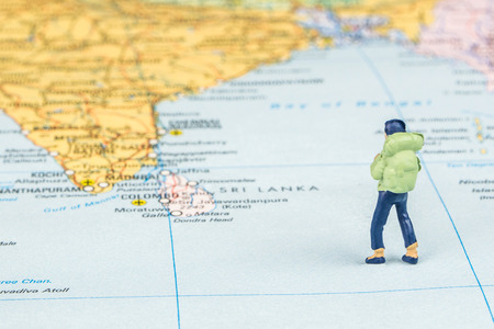 closeup of miniature figurine of young traveller standing on big map next to Sri lanka islandsの写真素材