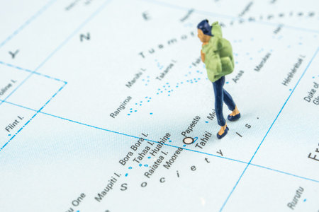 closeup of miniature figurine of young traveller standing on big map next to Tahiti islandsの写真素材