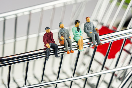 miniature figurines sitting on the edge of shopping cart while having business team meetingの写真素材