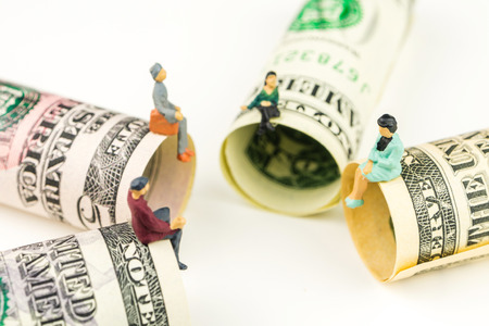 miniature figurines sitting on the edge of 100 dollar banknote on white backgroundの写真素材