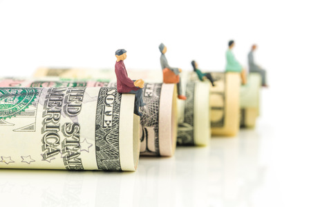 miniature figurines sitting on the edge of us dollar banknotes on white backgroundの写真素材