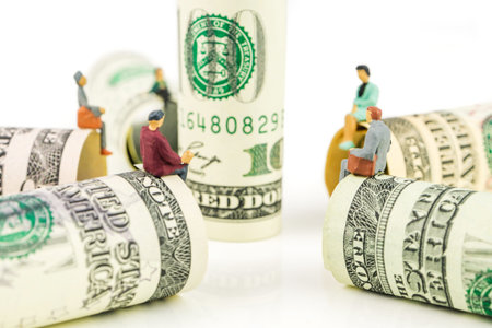 miniature figurines sitting on the edge of dollar banknote on white background