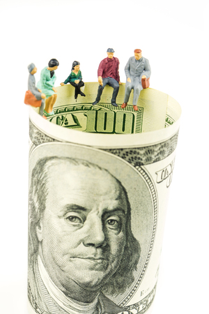 miniature figurines sitting on the edge of 100 dollar banknote on white backgroundの写真素材